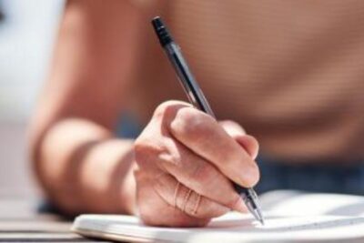 Persona escribiendo propósitos de Año Nuevo en una libreta, representando los retos para cumplir metas personales.