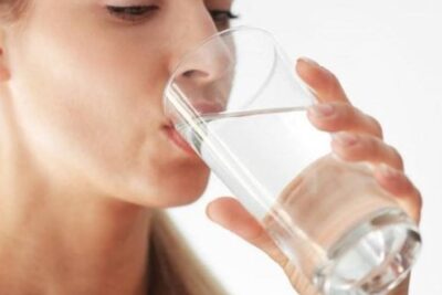 Mujer bebiendo un vaso de agua, simbolizando la importancia de mantenerse hidratado para la salud y la longevidad.