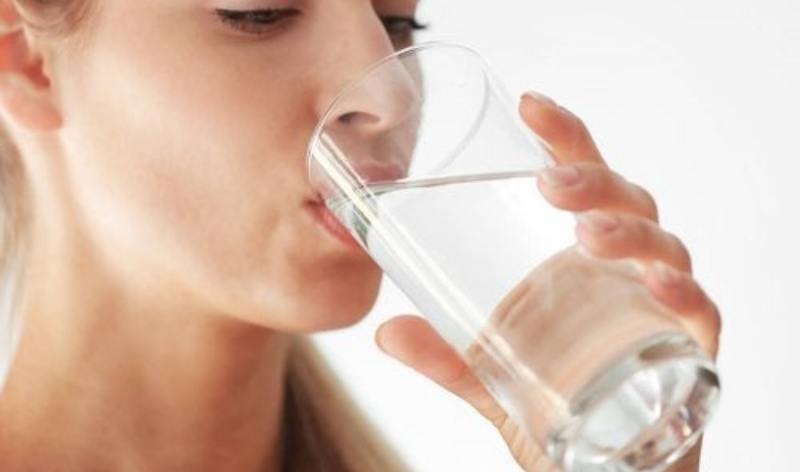 Mujer bebiendo un vaso de agua, simbolizando la importancia de mantenerse hidratado para la salud y la longevidad.