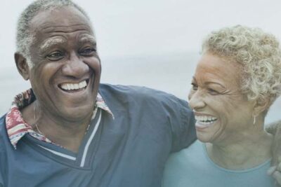 Dos personas mayores sonriendo en un entorno natural, simbolizando vitalidad y bienestar, teniendo un envejecimiento saludable.