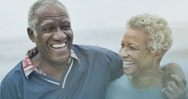 Dos personas mayores sonriendo en un entorno natural, simbolizando vitalidad y bienestar, teniendo un envejecimiento saludable.